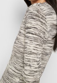 Stickad tröja i ett off-white och svart abstrakt mönster. Har rund halsringning och långa raglanärmar.