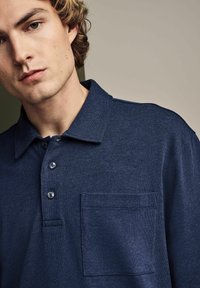 Marineblaue Polo-Shirt aus strukturiertem Stoff, mit drei Knöpfen, umgeschlagenem Kragen und Brusttasche.