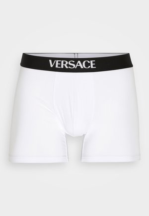White boxer briefs with a black elastic waistband featuring "VERSACE" in white lettering. Smooth texture, fitted design, and mid-thigh length.