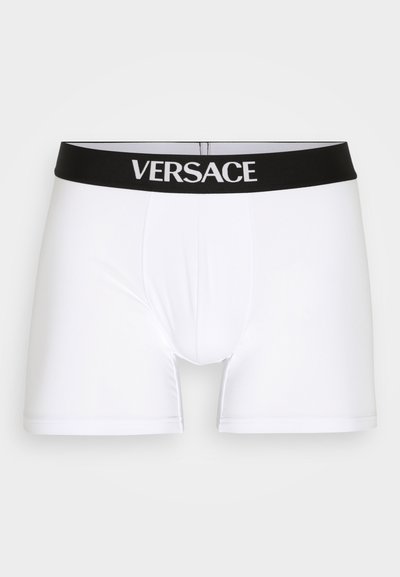 Fehér boxeralsó fekete gumis derékkal, amelyen fehér betűkkel "VERSACE" felirat található. Sima textúra, testhezálló design és combközép hossz.