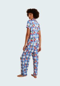 Blue checkered pajama set with red cherry print. Short-sleeved top and loose-fitting pants feature a playful pattern with a soft texture.