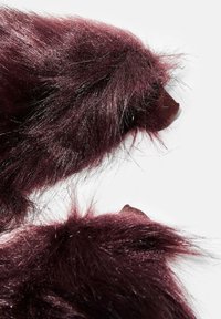 Burgundy falsk pels, lang og fluffy tekstur, med markante mørke nuancer. Produktet har en glat stofbund til fastgørelse.