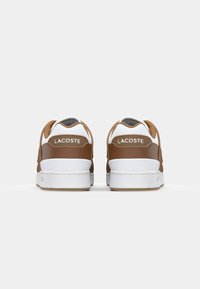 Brown leather sneakers with white rubber soles. Features a textured design and subtle Lacoste branding on the heel. Clean, modern shape.
