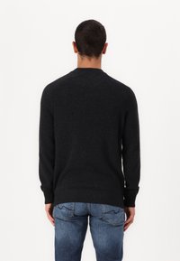 Mørk grå strikkegenser med rund hals, lange ermer og ribbestrikket kant. Brukt med blå denimjeans, sett fra baksiden.