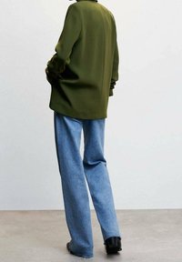 Blazer vert à coupe structurée avec des épaules marquées, associé à un jean denim bleu clair à jambes larges, et des bottines noires.
