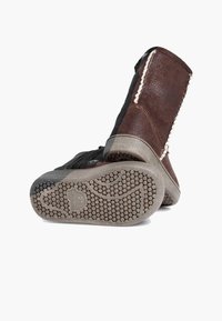 Botas de cuero marrón con una superficie texturizada, que cuentan con una sección negra contrastante y una suela de goma con patrones de agarre.