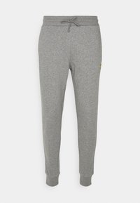 Schmal geschnittene graue Jogginghosen mit einem Kordelzugbund und elastischen Bündchen, mit einem kleinen gelben Logo auf dem rechten Oberschenkel.