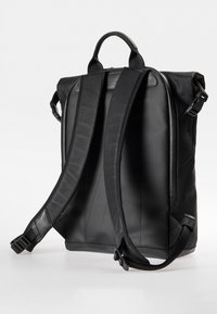 Zaino in pelle nera con spallacci imbottiti regolabili e manico superiore. Presenta un design elegante e una superficie liscia, con hardware minimale.