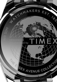 Montre argentée avec un cadran noir arborant un design de globe. Le texte inclut "WR 50M", "WATCHMAKERS EST. 1854", et "DESIGNED & ENGINEERED by TIMEX."