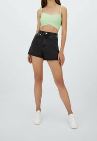 Mintunvihreä lyhyt toppi, jossa ohuet hihnat, yhdistetty korkeavyötäröisiin mustiin farkkushortseihin, joissa on karhea helma. Malli käyttää valkoisia tennareita.