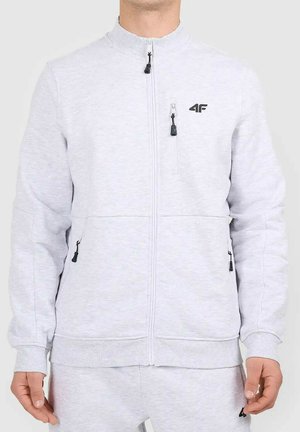 Mężczyzna noszący jasnoszary sweter na suwak z czarnymi suwakami i logo 4F na piersi, w połączeniu z pasującymi spodniami dresowymi.