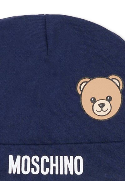 Cappellino di lana blu navy con una piccola toppa raffigurante un orsetto sorridente e la scritta bianca "MOSCHINO" stampata sotto l'orsetto sul davanti.