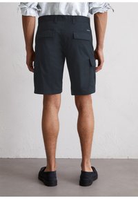 Pantalones cortos de carga en color azul marino con bolsillos laterales, cinturilla ajustable, tejido ligero y un ajuste relajado, combinados con zapatos negros sin cordones.