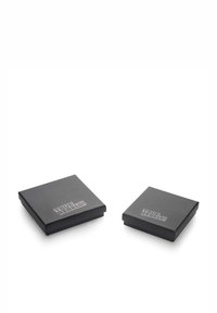 Divi kvadrātveida dāvanas iepakojumi matē melnā krāsā ar izvirzītu sudraba logo "TRUE REBELS!" uz augšējās virsmas. Viens iepakojums ir nedaudz mazāks par otru.