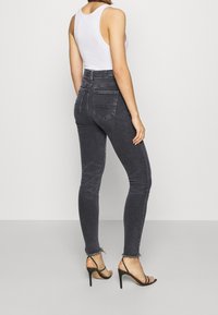 High-waisted, dark grey skinny jeans with frayed hem and two back pockets, paired with a white tank top and black strappy heels.