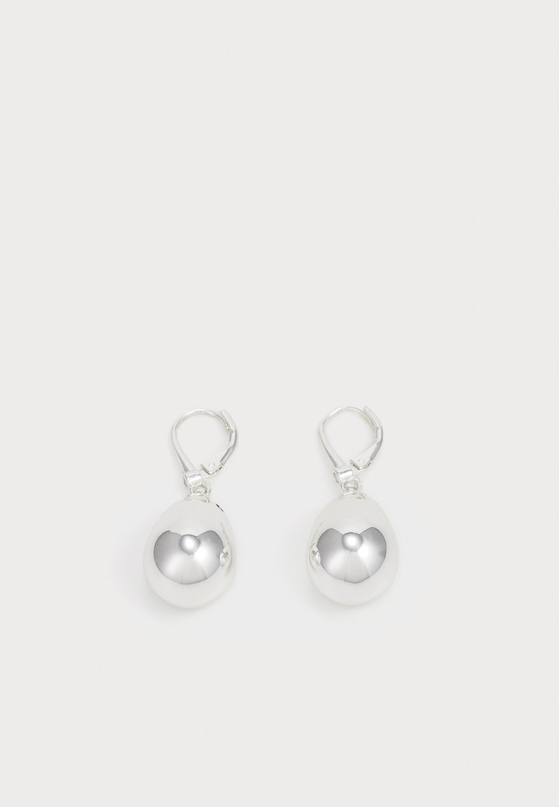 Silver hängande örhängen med släta, runda, reflekterande ytor som hänger från spännen med lyftback. Bakgrunden är helt vit.