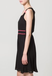 Robe noire sans manches avec une taille cintrée, dotée de bretelles accentuées roses et d'une jupe fluide. Texture lisse et longueur au genou.