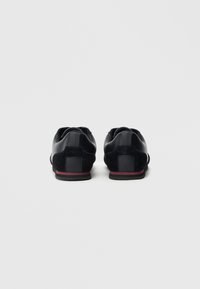 Sapatos pretos com parte superior em couro liso, detalhes em camurça e sola vermelha de borracha. Apresentam um detalhe de salto quadrado e design minimalista.