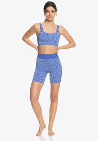 Conjunto deportivo de color azul con un diseño estampado que incluye una camiseta corta sin mangas con tirantes anchos y unos pantalones cortos de cintura alta, ambos con un diseño de diamantes texturizados.