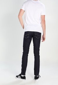 Jean slim bleu foncé avec un design à cinq poches, assorti à un t-shirt blanc et des baskets noires avec trois bandes blanches.
