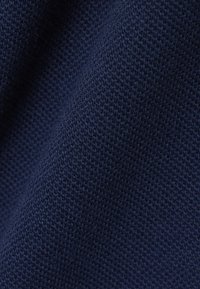 Nahaufnahme eines dunkelblauen Strickstoffs mit einer strukturierten, waffelähnlichen Musterung und weichen Falten, die Schatten erzeugen.