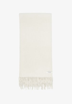 Soft cream-colored scarf with twisted fringe edges and a small white label reading comma est. 1973 on one corner.