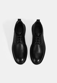 Zwarte leren schoenen met een gestructureerde afwerking, ronde neuzen, vetersluiting en subtiele stikdetails. Platte zolen en trekhandvatten aan de achterkant.
