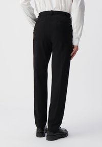 Zwarte broek met een relaxte pasvorm, voorzien van een elastische tailleband, twee achterzakken en een gladde stoftextuur. Gekocht met zwarte schoenen.