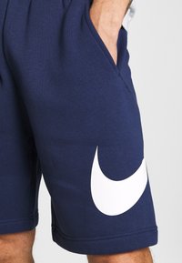 Pantaloni sportivi bleu navy realizzati in tessuto morbido, con un grande logo bianco della Nike sul lato, dotati di tasche laterali e vita elastica.