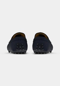 Par plave suede mokasina s crnim gumiranim čepovima na petama i potplatima, prikazani odostraga na bijeloj pozadini.