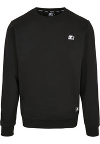 Sweat-shirt noir col rond à manches longues, petit logo blanc sur la poitrine gauche, et un écusson de marque près de l'ourlet inférieur.