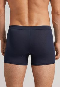 Tmavě modré trenýrky vyrobené z hladkého textilu, s těsným střihem a širokým pasem, s minimálními detaily šití.