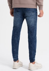 Joggers en denim bleu délavé moyen, dotés de poignets élastiqués et de deux poches arrière, avec une texture lisse et un design fuselé.