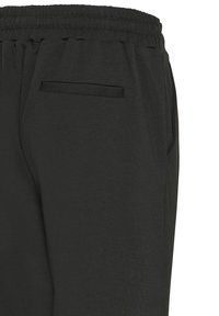 Pantaloni con elastico in vita neri, tasca posteriore a filetto e cucitura laterale visibile su sfondo semplice.
