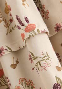 Floral cotton fabric with a light beige background, featuring pink, purple, and green plant illustrations and visible stitching details.