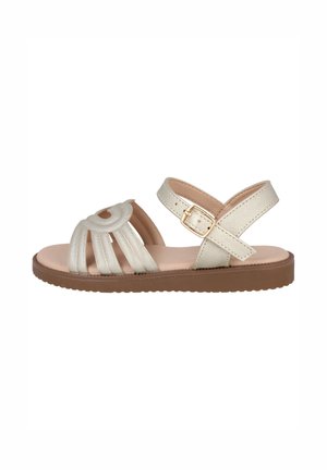 Sandalia beige de punta abierta con una suela plana marrón, múltiples correas delanteras y una correa ajustable en el tobillo con una hebilla dorada.