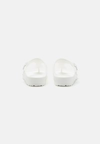 Hvite sandaler med glatt syntetisk materiale, åpen bakdesign, teksturert såle og justerbar stropp på siden.