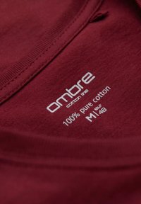 Burgundské bavlněné tričko s kulatým výstřihem. Obsahuje bílou tištěnou etiketu s nápisy "ombre", "100 % čistá bavlna" a velikost "M 48".