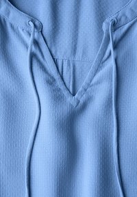 Sweat à capuche bleu clair avec un design en V, en tissu texturé présentant de petits points en relief, et des cordons de serrage le long de l'encolure.