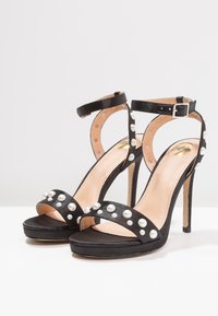 Czarne sandały na wysokim obcasie z perłowymi zdobieniami, z cienkim paskiem na kostce i gładką skórzaną fakturą na eleganckiej podeszwie.
