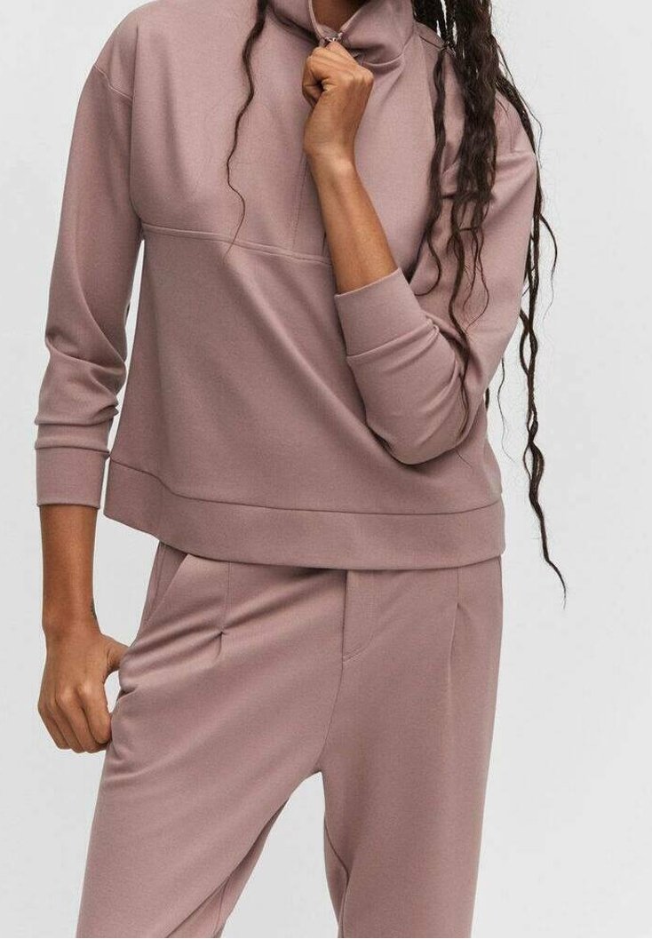 Conjunto de ropa de descanso en malva claro, hecho de tela suave, que incluye una sudadera de cuello alto y pantalones ajustados con bolsillos laterales y un ajuste cómodo.