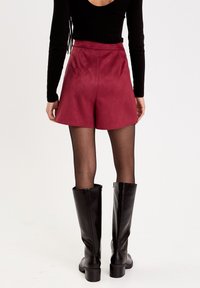 Czerwone krótkie spodenki z sztucznego zamszu o wysokim stanie i rozkloszowanym kroju, w połączeniu z czarnymi kozakami za kolano i czarną bluzką z długim rękawem. Gładka faktura.