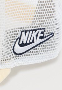 Tela de malla blanca con un logo de Nike bordado en negro y blanco con el swoosh sobre un fondo claro.