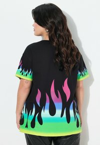Camiseta negra con gráficos de llamas coloridos en rosa, azul y verde, con mangas cortas y un corte relajado.