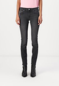 Jeans ajustados negros con cintura alta, diseño de cinco bolsillos y un ligero desgastado. Hechos de mezclilla, combinados con botas negras hasta el tobillo.