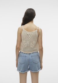 Top de punto color crema sin mangas con patrón de calados, straps ajustables y emparejado con shorts de mezclilla azul claro con dobladillos enrollados y bolsillos traseros.