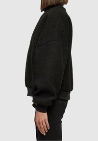 Maglione in pile nero con collo alto, vestibilità oversize e superficie testurizzata; presenta polsini e bordo a coste per una maggiore struttura.