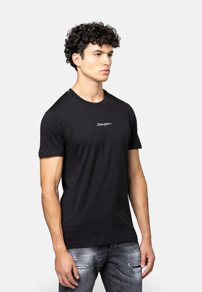 Zwarte katoenen t-shirt met korte mouwen, ronde hals en subtiele witte logo op de voorkant, gecombineerd met versleten lichtblauwe jeans.