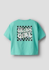 Camiseta corta verde menta con un diseño gráfico que incluye las palabras "DREAM GIRL", flores, corazones y un fondo de tablero de ajedrez en blanco y negro.
