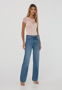Body rosa chiaro con maniche corte e design a zig-zag, abbinato a jeans di denim blu a vita alta e sandali con tacco nudo.